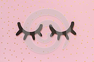 Decorative black wooden eyelashes, closed eyes and gold stars on pink background. Concept Good night or Sweet dreams Greeting card