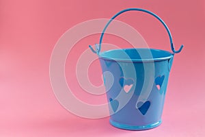 Decorative blue bucket with heart shaped holes on pink background. Festive concept