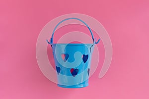 Decorative blue bucket with heart shaped holes on pink background. Festive concept