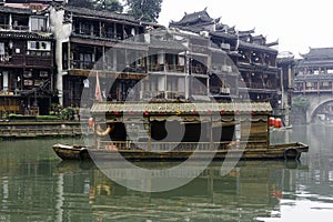 A decorative boat floats in the Tuo Jiang River in front of residential apartments in the quaint village of Fenghuang Ancient City