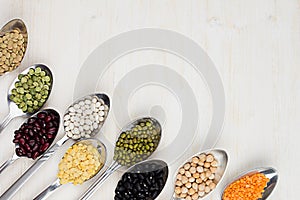 Decorative border of assortment pulses beans in spoons with copy space on white wood background.