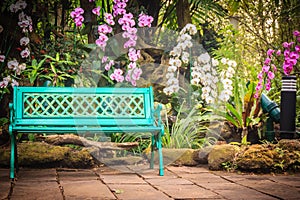 Decorative bright blue bench on concrete brick floor with beautiful orchid flowers and green garden background. Peaceful garden d