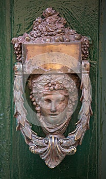 Decorative bronze door handle in the form of a beautiful woman`s head on a green painted door. Malta