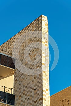 Decorative building facade with stones and rock tiles in late afternoon sun and shade with metal balconies and walkways