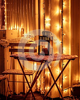 A decorative candle lantern burning on the table covered with snow. Christmas time, winter night, no people.