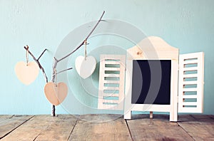 Decorative chalkboard frame and wooden hanging hearts over wooden table. ready for text or mockup. retro filtered image