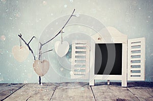 Decorative chalkboard frame and wooden hanging hearts over wooden table. ready for text or mockup. retro filtered image