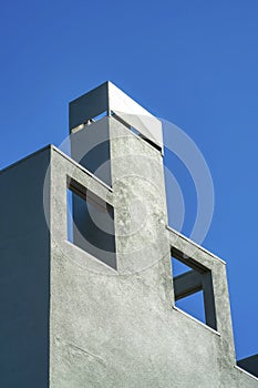 Decorative chimney facade with openings and metal top with gray or blue stucco exterior in the late afternoon sunshine