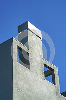 Decorative chimney facade with openings and metal top with gray or blue stucco exterior in the late afternoon sunshine photo