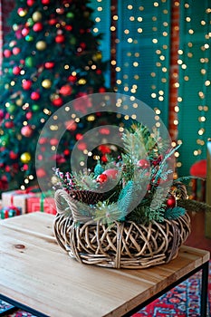 The decorative Christmas basket is located on a table on the background of a Christmas tree.