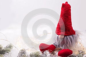 Decorative christmas elf or gnome with fairy lights and fir tree branches on white fur background