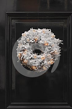 Decorative Christmas wreath covered in artificial snow with illuminated gold colored baubles attached to a green door of a house