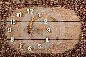 Decorative clock with wooden numerals and arrows made of cinnamon sticks, showing 3 o`clock, on a wooden background and a frame of