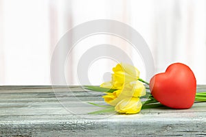Decorative composition of yellow tulips and a red heart on rustic bright wooden table. Concept card. Mothers day.