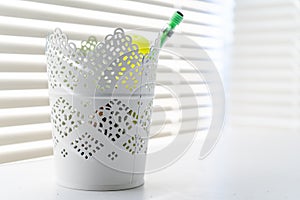 Decorative container used as a pencil holder in a home office, against a window, with sunbeams and white home decor