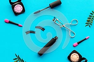 Decorative cosmetic set with lash curler and mascara on blue woman desk background top view
