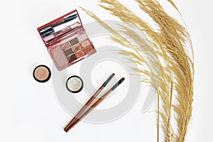 Decorative cosmetics, eye shadow, makeup brushes and a bouquet of dry grass