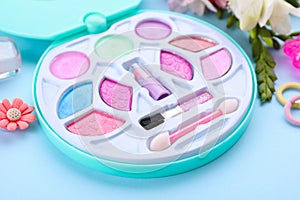 Decorative cosmetics for kids. Eye shadow palette, accessories and flowers on light blue background, closeup