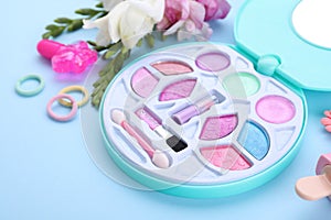 Decorative cosmetics for kids. Eye shadow palette, accessories and flowers on light blue background, closeup