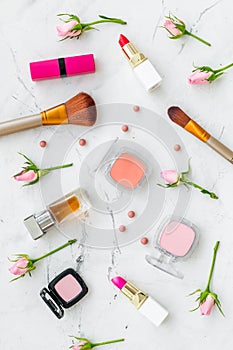 Decorative cosmetics layout. Pink tones of lipstick, bulk, eyeshadow, perfume, brushes among rose flowers on white