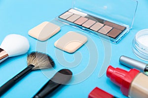 Decorative cosmetics, makeup products and brushes on blue background