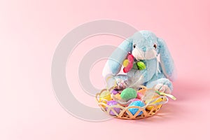 Decorative Easter eggs with feathers in basket and soft toy rabbit on pink background. Easter composition, greeting card with