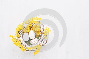 Decorative Easter eggs and mimosa wreath on a white background. Flat lay, copy space