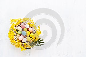 Decorative Easter eggs in mimosa wreath on a white background. Top view, copy space