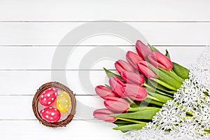 Decorative Easter eggs in nest and red tulips on white wooden table. Copy space, top view.Decorative Easter eggs in nest and red t