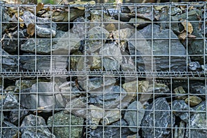 Decorative fence of bulk stone in the grid. Textured background of a stone wall with iron netting. Stone wall in wire frame.