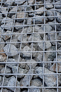 Decorative fence of bulk stone in the grid. Textured background of a stone wall with iron netting.Gabion filled with limestone