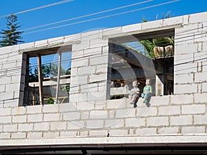 Decorative figures of a boy and a girl sit in the window opening of a house under construction made of white brick