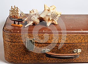Decorative figurine of a ship, seashells on an old leather suitcase isolated on a white background.