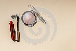 Decorative flat lay composition with cosmetic powder, brush, mascara on beige background. Hard light. Cosmetics and