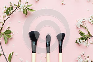 Decorative flat lay composition with cosmetics brushes and flowers. Flat lay, top view on pink background