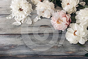 Decorative floral frame, banner made of pink and white peonies flowers. Old grey wooden table background. Empty copy