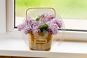 Decorative flower basket with branches of spring lilacs on the windowsill of a country house. the concept of a good spring mood