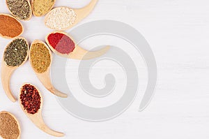 Decorative flower ornament of different spices in bamboo spoons on white wood background, top view, closeup.