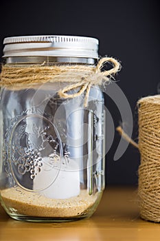 Decorative glass jar with twine spool against black on wood