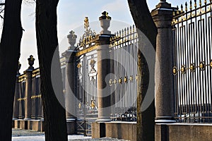 Decorative grille with gilded ornaments and granite columns in the rays of the setting sun