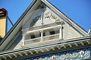Decorative hidden balcony with victorial style and fancy facade on exterior with gable roof and blue sky background in