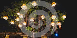 Decorative illuminated lighting of many vintage bamboo lamps with chicken coops hanging on trees in night garden