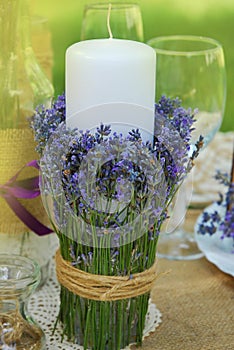 Decorative Lavender Glass, with Lavender Flowers with Candle on a table and Green Blured Summer Bakground.