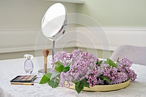 Decorative makeup cosmetics, table mirror and fresh lilac flowers
