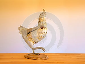 Decorative metalic rooster on wooden table.