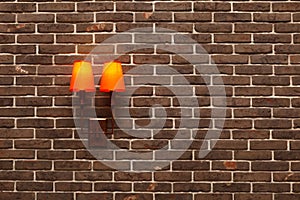 Decorative, neat wall made of brown ceramic bricks and wall lamps with orange shades