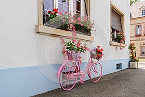 A decorative old pink bicycle with a flower basket near a building in a small French city