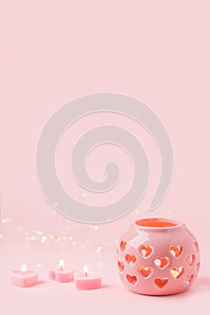 Decorative pink ceramic lanterns with heart cutouts lit by glowing candles onpink background, copy space, Saint Valentine, Mother