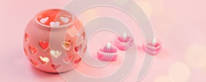 Decorative pink ceramic lanterns with heart cutouts lit by glowing candles onpink background, copy space, Saint Valentine, Mother