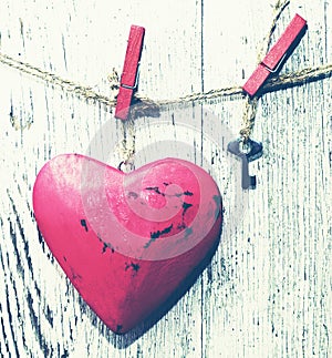 Decorative red heart and small metal key on a rope against the background of an old white board